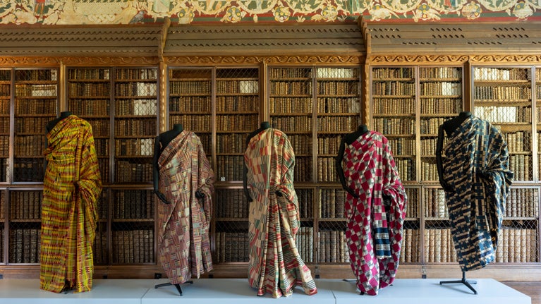 Five mannequins line up against a bookcase at Blickling, wearing colourful African textiles